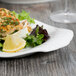 A Libbey white porcelain platter with food including a piece of fish and a lemon wedge on it.