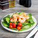 A Libbey round porcelain plate with shrimp and spinach salad on it.