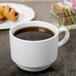 A Libbey white porcelain tea cup filled with coffee on a table with pastries.