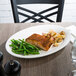 A Libbey white porcelain platter with food including green beans and potatoes on a table.