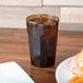 A Cambro amber plastic tumbler filled with brown liquid on a table next to a plate of food.