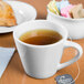 A white Libbey porcelain tea cup filled with tea sits on a table next to a plate of pastries.