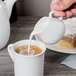 A person pouring milk from a Libbey Royal Rideau white creamer into a cup of coffee.