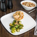 A Libbey white square porcelain plate with a meat pie and brussels sprouts on a table.
