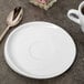 A white porcelain saucer with a cup of coffee on a table.