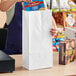 A woman putting a box of food into a white tall paper bag.