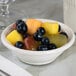 A Tuxton Hampshire eggshell embossed china fruit dish filled with fruit on a table.