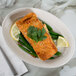 A Tuxton Hampshire oval china platter with a piece of salmon and green beans and a lemon wedge on it on a marble table.