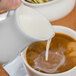 A person pouring milk into a cup of coffee using a Libbey Royal Rideau white porcelain creamer.