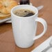 A close-up of a white Libbey porcelain mug filled with brown liquid on a table with a spoon.