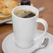 A close-up of a white Libbey mug with brown liquid on a saucer.