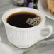 A Tuxton eggshell embossed short cup of coffee on a white saucer with a spoon.