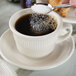 A person using a spoon to pour sugar into a Tuxton Hampshire short cup of coffee.