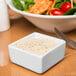 A square white Libbey Royal Rideau ramekin filled with white sauce on a table with a fork.