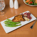 A plate of food with a fork and a glass of water on a Libbey rectangular porcelain tray.