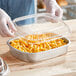 A person holding a Durable Packaging aluminum tray of macaroni and cheese with a dome lid.