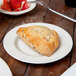 A Reserve by Libbey Royal Rideau white medium rim porcelain plate with a pastry on it and a bowl of strawberries on the table.