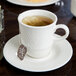 A Reserve by Libbey Royal Rideau white porcelain tea saucer with a cup of tea and a tea bag on it.