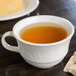 A Reserve by Libbey Royal Rideau white porcelain tea cup filled with tea sits on a saucer on a table.