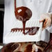 A person using a Martellato Polycarbonate chocolate mold to pour liquid chocolate into a container.