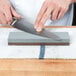 A hand using a Victorinox Norton combination coarse/fine stone to sharpen a knife.