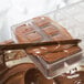 A Chocolate World polycarbonate chocolate mold with a wooden square shape being poured into.