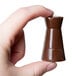 A hand holding a small brown Matfer Bourgeat chess piece made of chocolate.