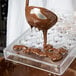 A person using a Matfer Bourgeat chocolate mold to pour liquid chocolate into heart-shaped compartments.