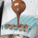 A chef using the Matfer Bourgeat Cannele Chocolate Mold to pour chocolate on a tray.