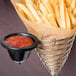 A Clipper Mill stainless steel wire mesh cone basket filled with french fries with a bowl of ketchup on a table.