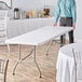 A man standing next to a Lancaster Table & Seating white rectangular table with a white tablecloth.