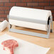 A Bulman steel paper dispenser with a roll of butcher paper on a white surface with a piece of meat.