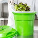 A person in a white coat and gloves mixing greens in a green Choice Prep salad spinner.