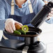 A person using an AvaMix Continuous Feed Juice Extractor to juice a kiwi into a bowl of fruit.