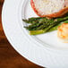 A plate of food with asparagus and meat served on a Homer Laughlin Kensington Ameriwhite china plate on a wood table.