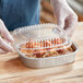 A person in gloves holding a Durable Packaging aluminum foil container of food.