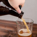 A hand pouring beer from a Libbey amber growler into a glass.