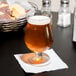 An Anchor Hocking Belgian beer glass full of beer with foam on a table.