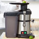 A person's hand holds a white plastic pulp collector with a black stripe over a juicer while squeezing lime juice into it.
