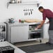 A man in a black apron putting eggs in an Avantco undercounter refrigerator.