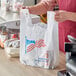 A person holding a white plastic "American Flag" t-shirt bag.