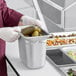 A person in gloves holding a Vollrath stainless steel steam table pan full of food.