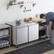 A man in a professional kitchen opening an Avantco undercounter refrigerator.