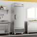 A stainless steel, single-door reach-in freezer on casters in a commercial kitchen setting.