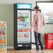 An Avantco black swing glass door refrigerator filled with bottles.