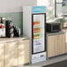 A white glass door merchandiser refrigerator with LED lighting, stocked with assorted beverages.