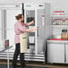 A man in an apron opening an Avantco reach-in freezer with a label on the door.