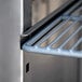 A metal shelf with a blue handle on a metal surface inside an Avantco stainless steel reach-in refrigerator.