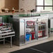 An Avantco stainless steel back bar refrigerator on a counter with bottles inside.