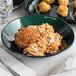 A green melamine bowl filled with spaghetti and meatballs on a marble table.